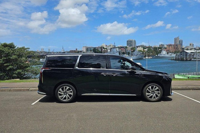 A black SUV parked in a parking lot with a city skyline and waterfront in the background. 1