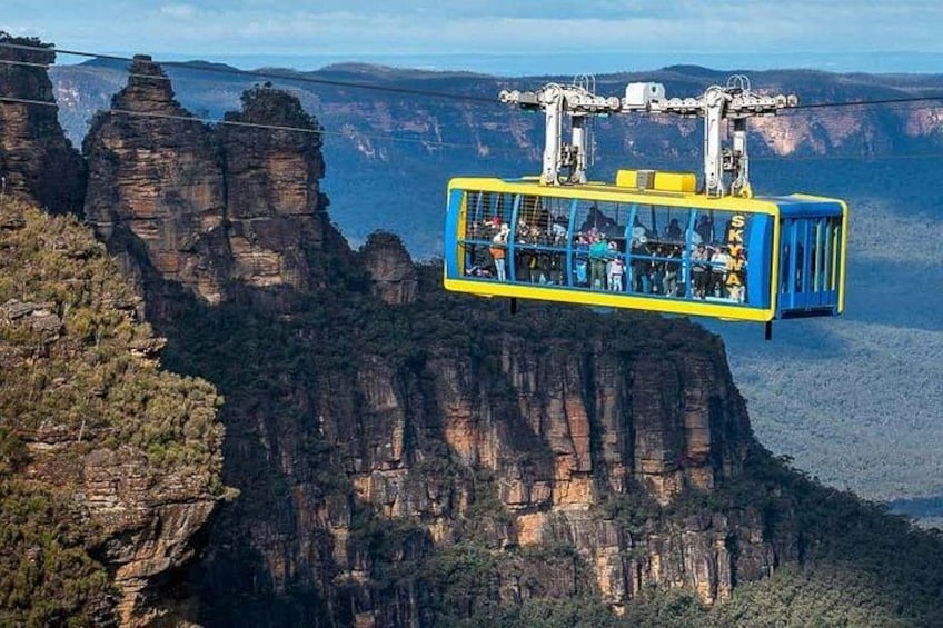A cable car suspended over a canyon with rocky cliffs and sparse vegetation. 5