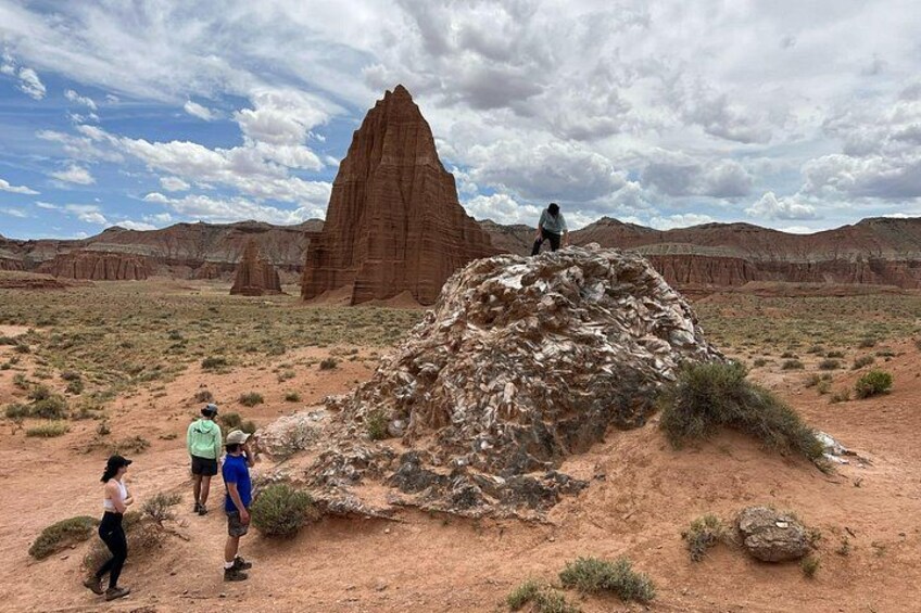 A desert landscape with a large rock formation, a smaller hill, and a group of people hiking. 4
