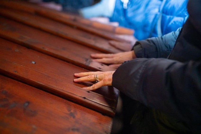 A wooden bench with hands resting on it. 2