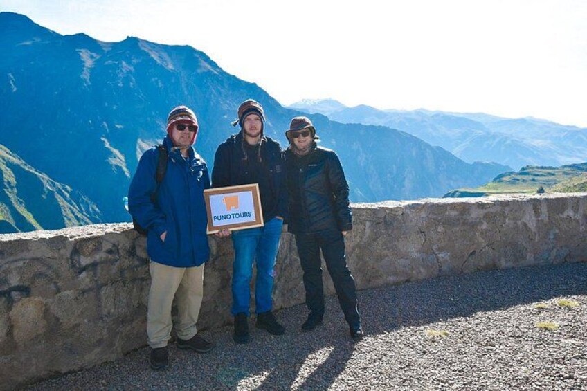 Three people standing on a rocky ledge with a mountainous landscape in the background. 4