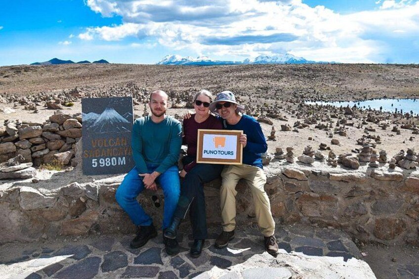 Three people sitting on a stone wall with a sign indicating the location of Volcan Sabancaya at 5980 meters. 3