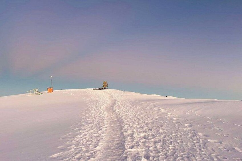 A snow-covered landscape with a clear sky, a path leading to a structure, and a small building on the left. 3