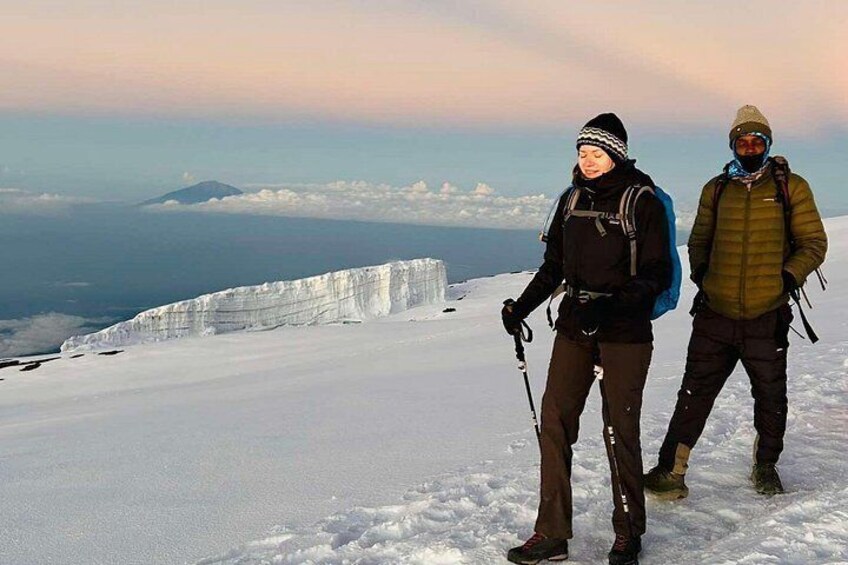 Two people hiking on a snow-covered mountain with a glacier in the background. 4