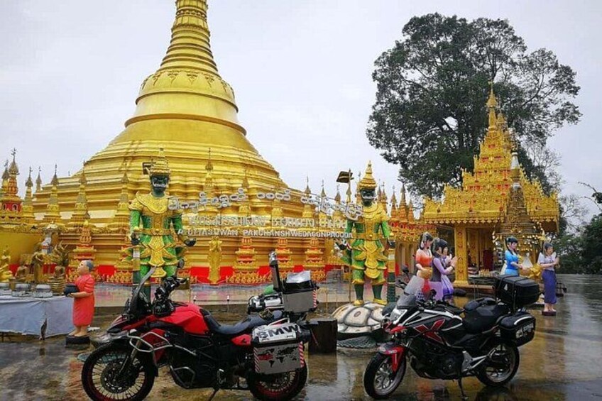 A golden stupa with a large statue in front, a motorcycle, and a temple in the background. 4