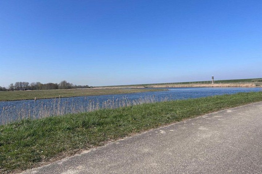 A paved road alongside a body of water with grassy banks and a clear blue sky. 3