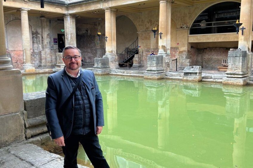 Un homme se tient près d’un bâtiment historique, avec une piscine verdâtre, des colonnes et un escalier. 2