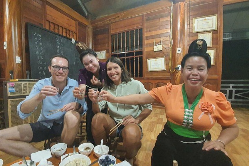 A group of people sitting at a table with food and drinks, in a room with wooden walls and a blackboard. 5