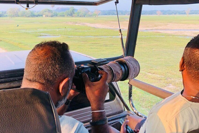 L'intérieur d'un véhicule où l'on voit une personne utilisant un appareil photo, une autre personne assise à côté, et une vue sur un champ verdoyant par la fenêtre. 4