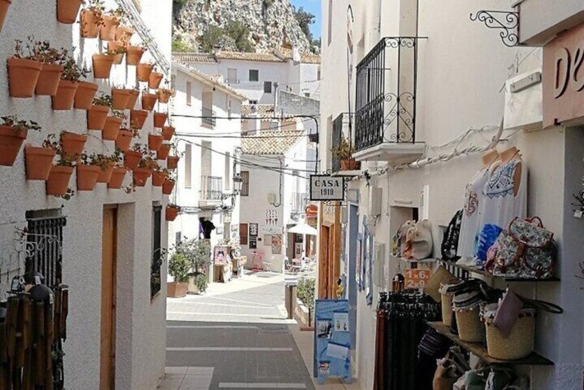 Une rue étroite, avec des pots en terre cuite sur le côté gauche, un magasin de vêtements sur le côté droit, et un bâtiment portant l’inscription « CASA 1918 » au loin. 4