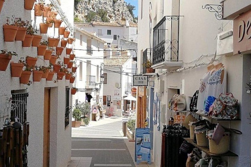 Una calle estrecha con macetas de terracota a la izquierda, una tienda de ropa a la derecha y un letrero que dice 'CASA 18' a lo lejos. 3