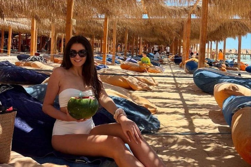 A person sitting on a beach lounge chair, holding a coconut. 1