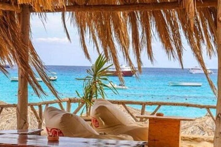 A beach with a thatched roof structure, a palm tree, and boats in the water. 3
