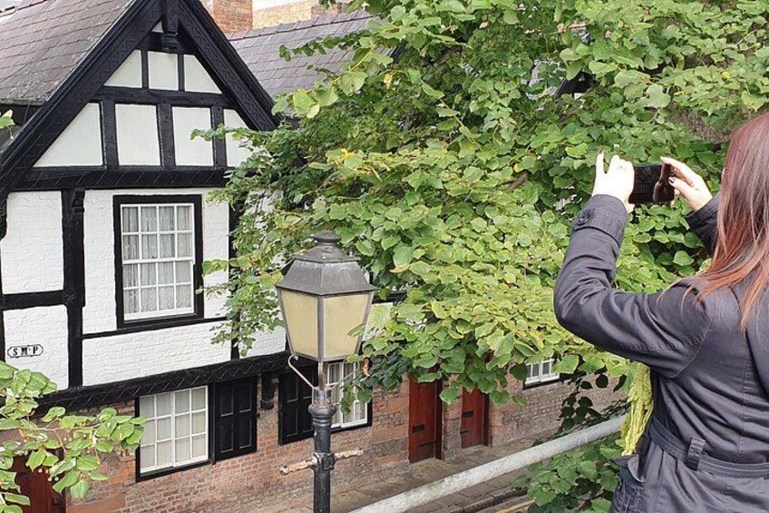 Una persona fotografiando un edificio de estilo Tudor con fachada blanco y negro, un farol y árboles cubiertos de hiedra. 2