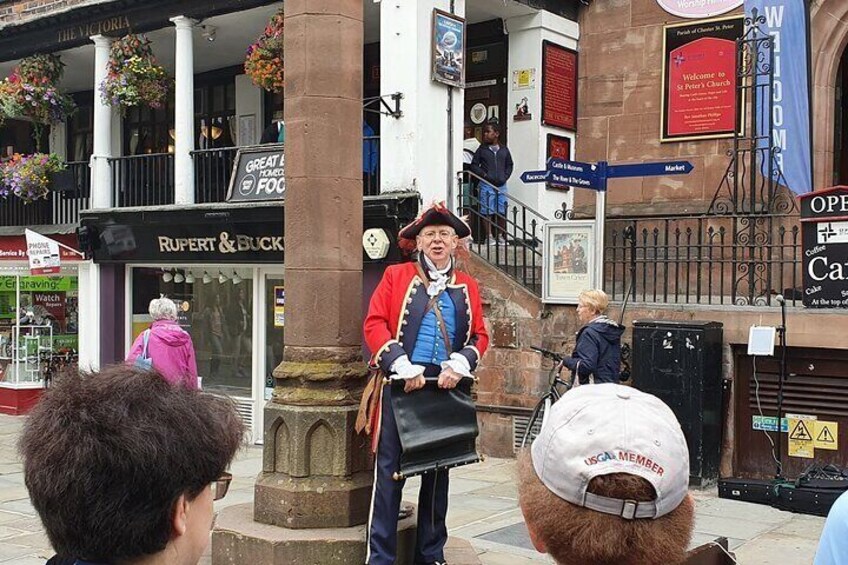 A person in a historical costume standing on a stone pedestal in a public square. 1