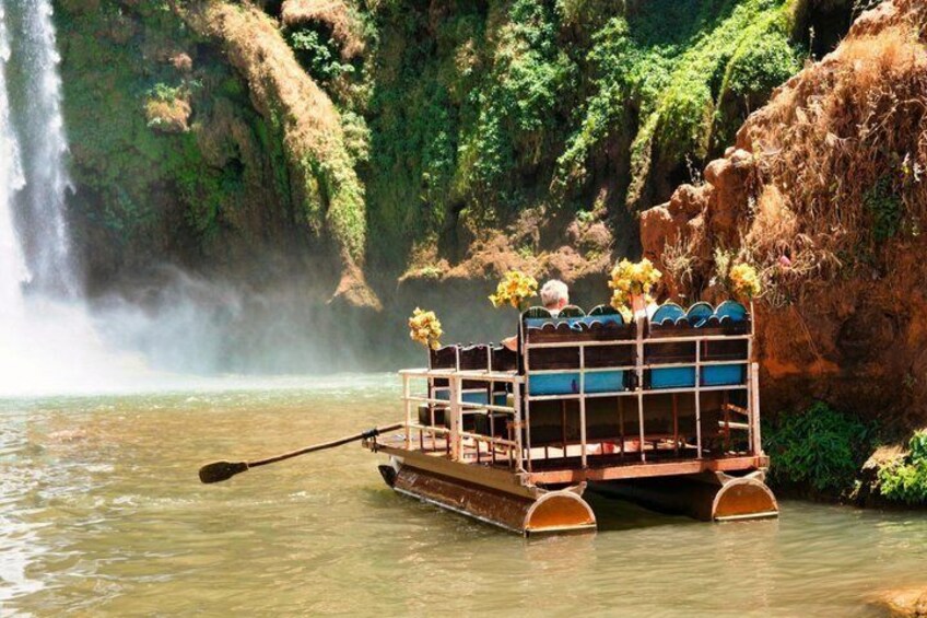 A boat with a wooden structure and flowers on the deck, floating on calm water with a waterfall in the background. 4