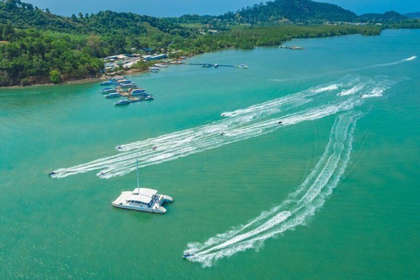 A clear turquoise sea with several boats, including a speedboat creating wake patterns, and a sailboat near the shore. 5