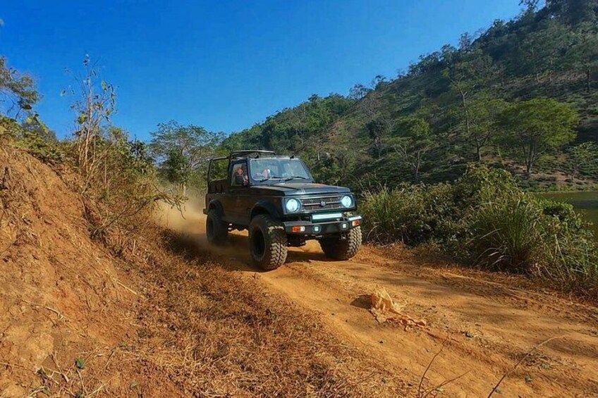 A vehicle driving on a dirt road surrounded by vegetation and hills. 4