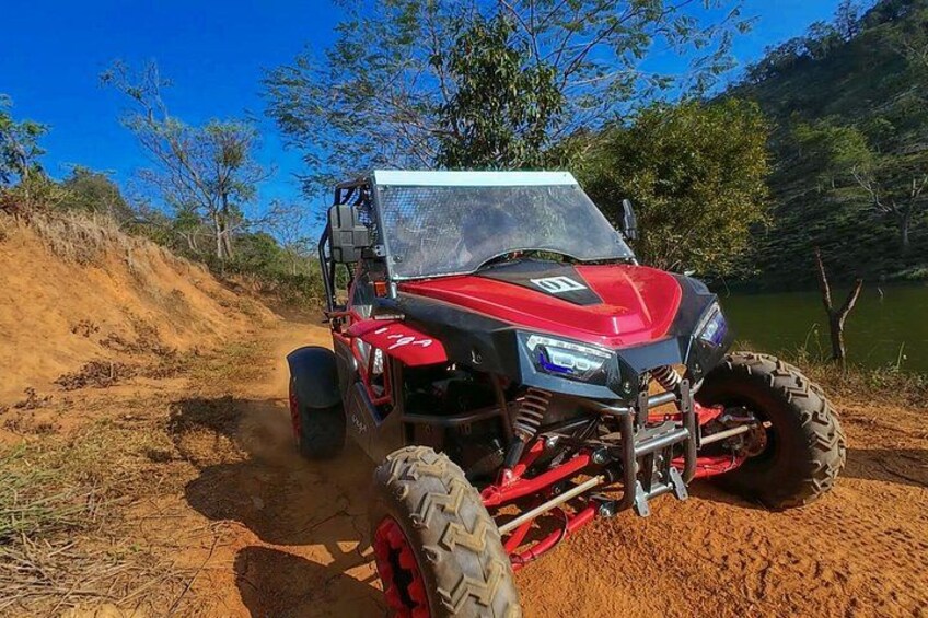 A red off-road vehicle on a dirt path with a lake and trees in the background. 2