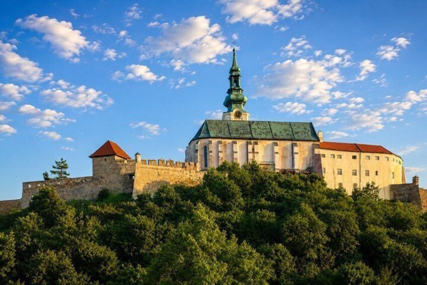 A historic building with a green spire, surrounded by lush greenery and a clear blue sky. 4