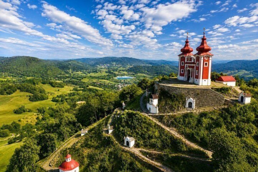 A red-roofed church with two domes on a hill, surrounded by lush greenery and a clear blue sky. 1