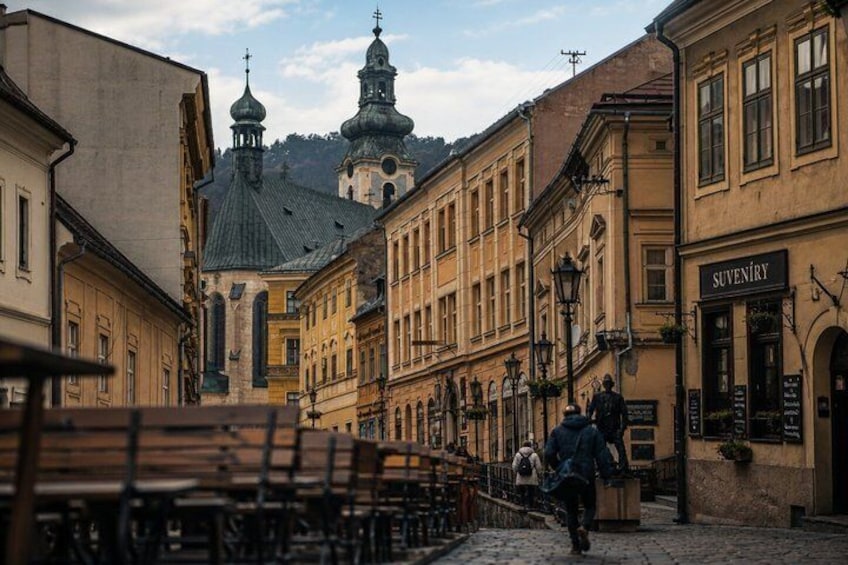 A cobblestone street with benches, historic buildings, and a church with domes. 2