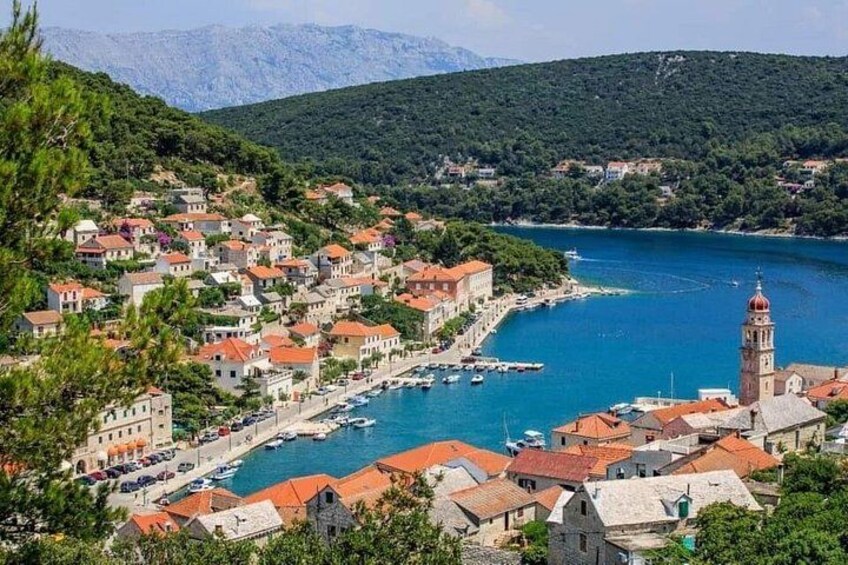 A coastal town with a prominent church tower, a marina with boats, and a mountainous backdrop. 3