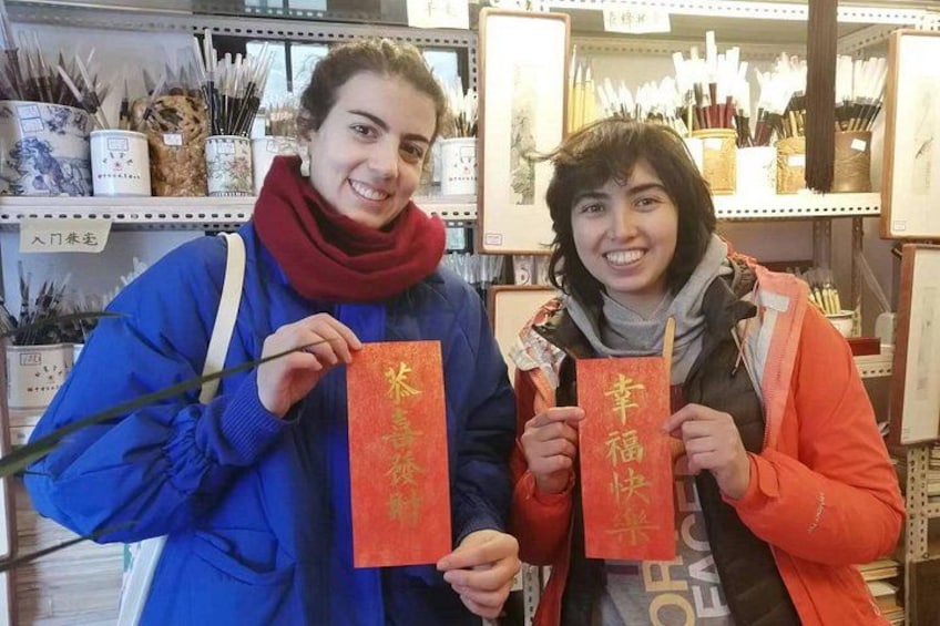 Two people holding red envelopes with gold characters, standing in a store with shelves of items. 1
