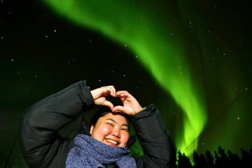 Una persona che forma un cuore con le mani sullo sfondo di un cielo notturno con aurore verdi. 2