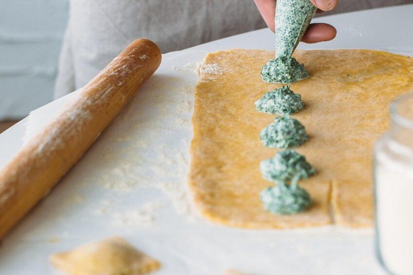 A person rolling dough with a rolling pin, applying green spread with a spoon, and a jar of milk on the table. 2