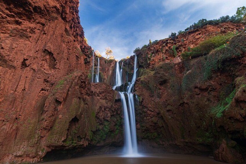 Una cascada escalonada que se precipita en una poza tranquila rodeada de acantilados rojizo-marrón. 5