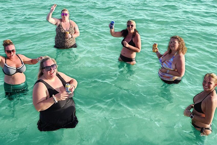 A group of people in clear turquoise water, some holding drinks. 3