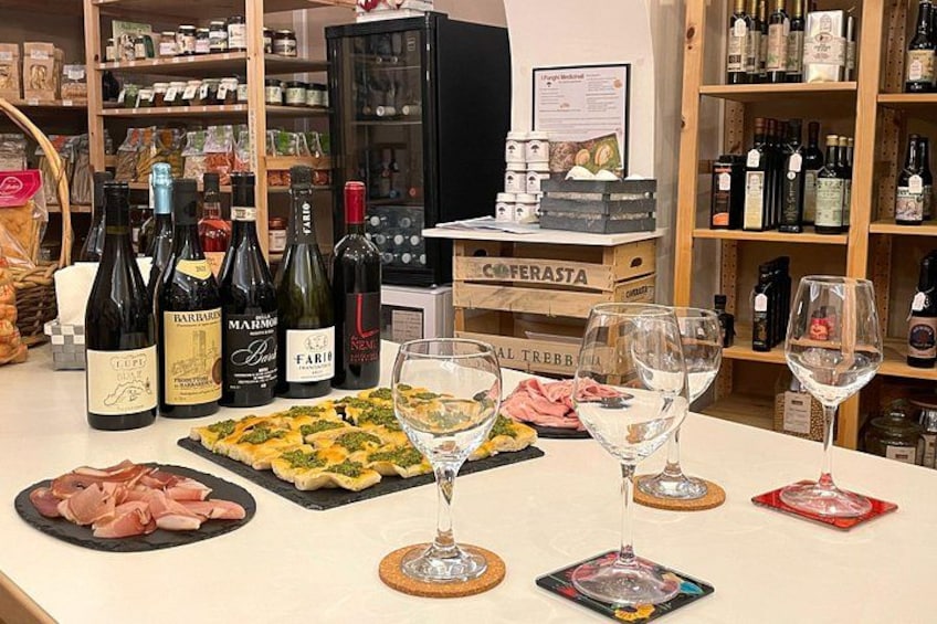 A wine tasting event with various bottles and glasses on a table, surrounded by shelves of wine bottles. 2