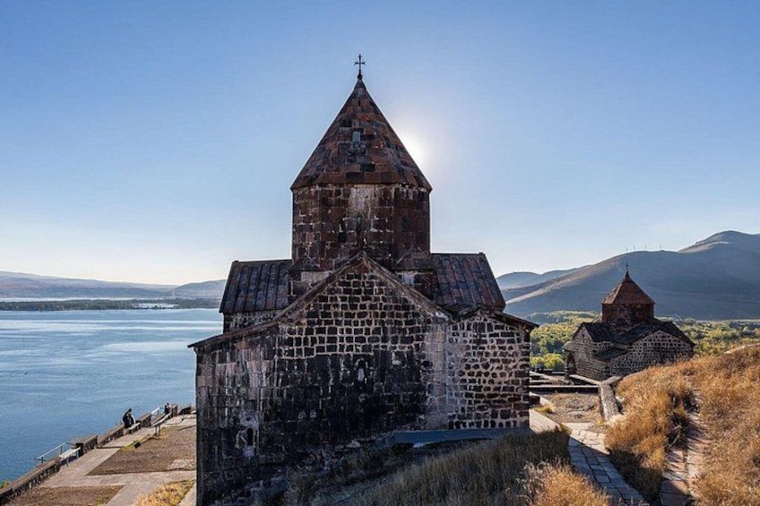 A stone church with a bell tower by a lake, surrounded by hills. 4