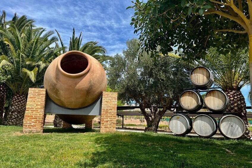 A large clay pot, several wooden barrels, and a palm tree in a grassy area. 1