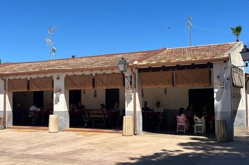 Un edificio con techo de tejas y puertas abiertas, personas sentadas en mesas afuera. 2