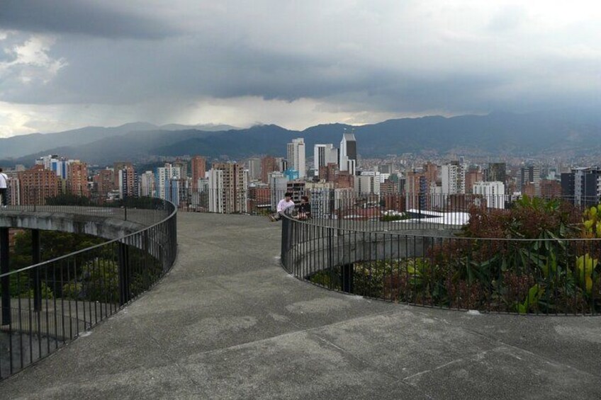 A concrete pathway with metal railings, leading to a cityscape with high-rise buildings and mountains in the background. 4