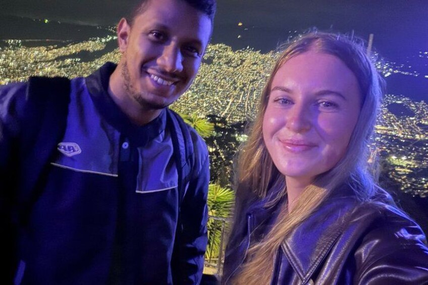 Two people standing outdoors at night with artificial lighting. 2