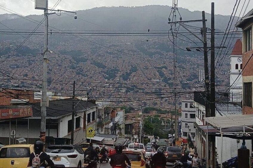 A busy street with vehicles and pedestrians, buildings, and a mountainous backdrop. 4