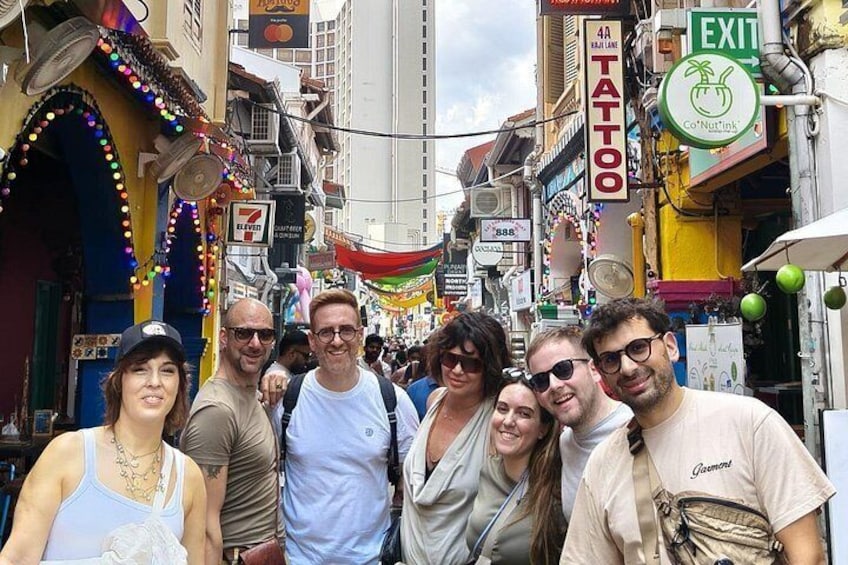 Un groupe de personnes se tient sur une rue animée, bordée de divers commerces et de nombreuses enseignes, dont un salon de tatouage et un magasin Co-Nutlink. 2