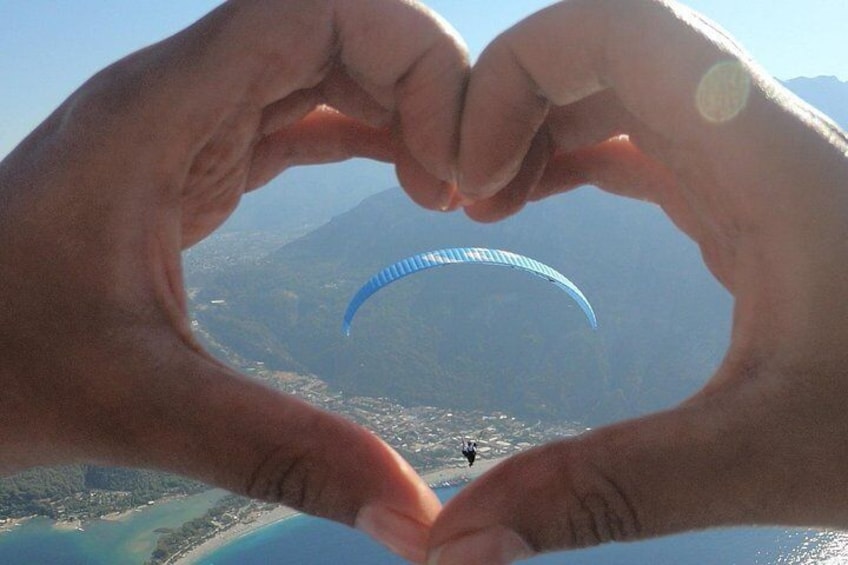 Une personne forme un cœur avec ses mains, et on aperçoit un parapente en arrière-plan. 4