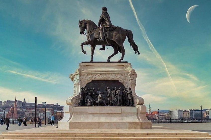 A statue of a man on horseback with a group of figures below, set against a cityscape with a crescent moon in the sky. 2