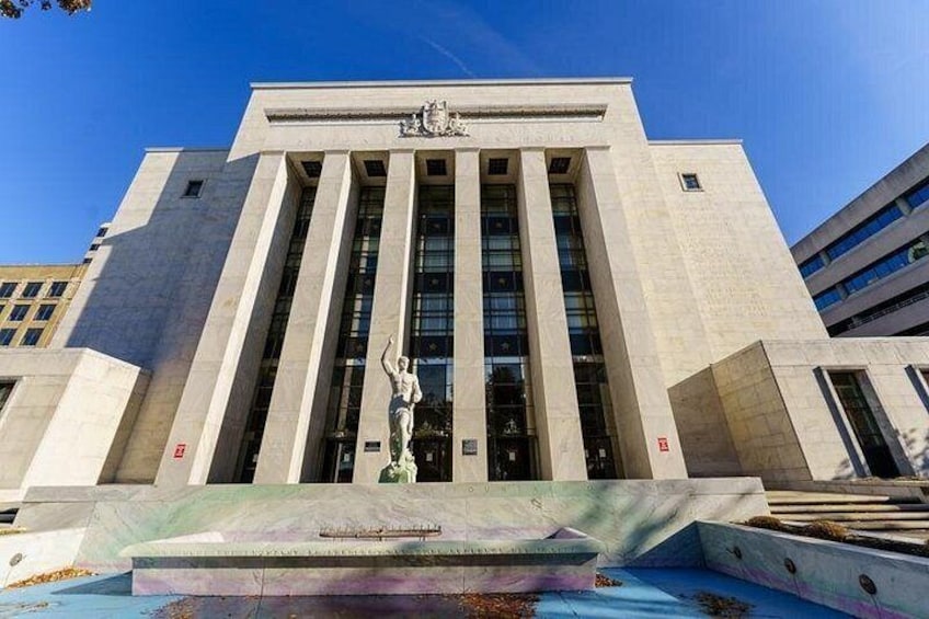 A large building with vertical columns and a statue in front. 2