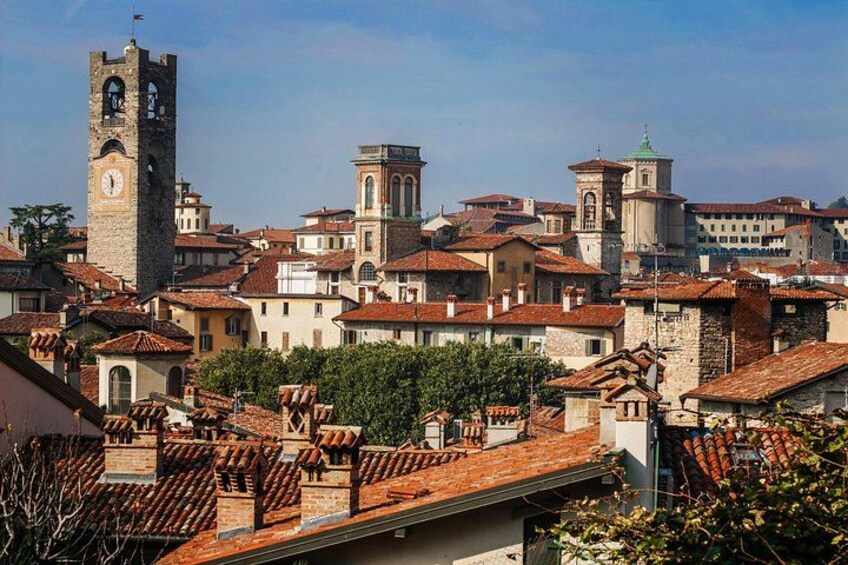 A historic town with a prominent clock tower, terracotta-roofed buildings, and a mix of stone and brick architecture. 1