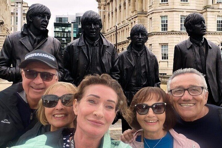 A group of people posing with a statue of a famous band. 3