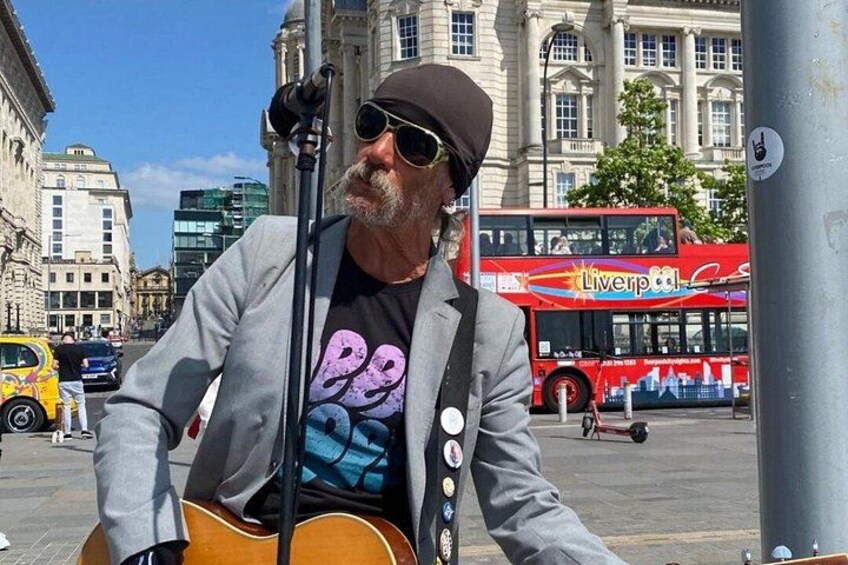 A man playing guitar on a city street with a double-decker bus in the background. 2