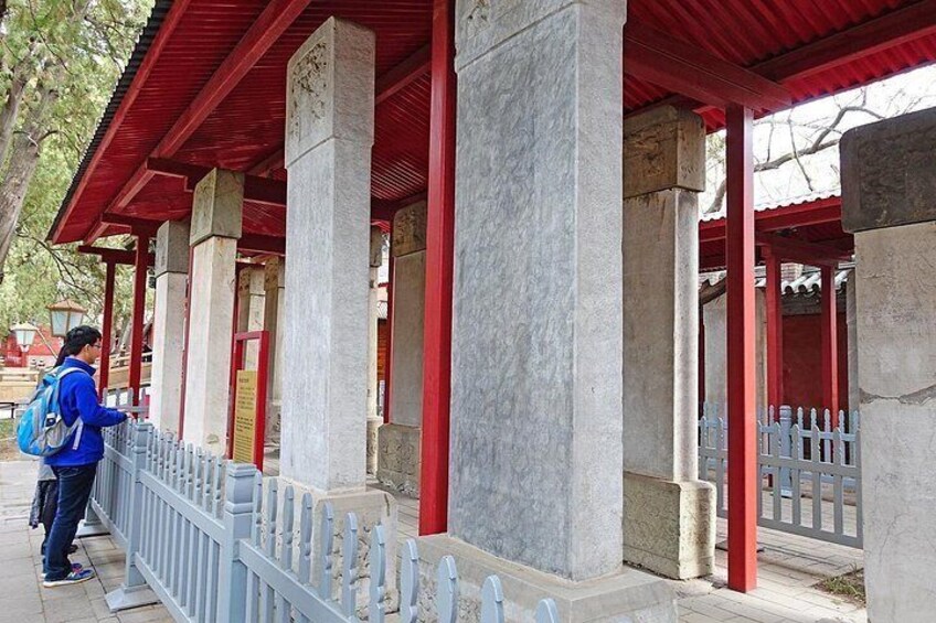 A person standing near a traditional structure with red pillars and a grey fence. 4