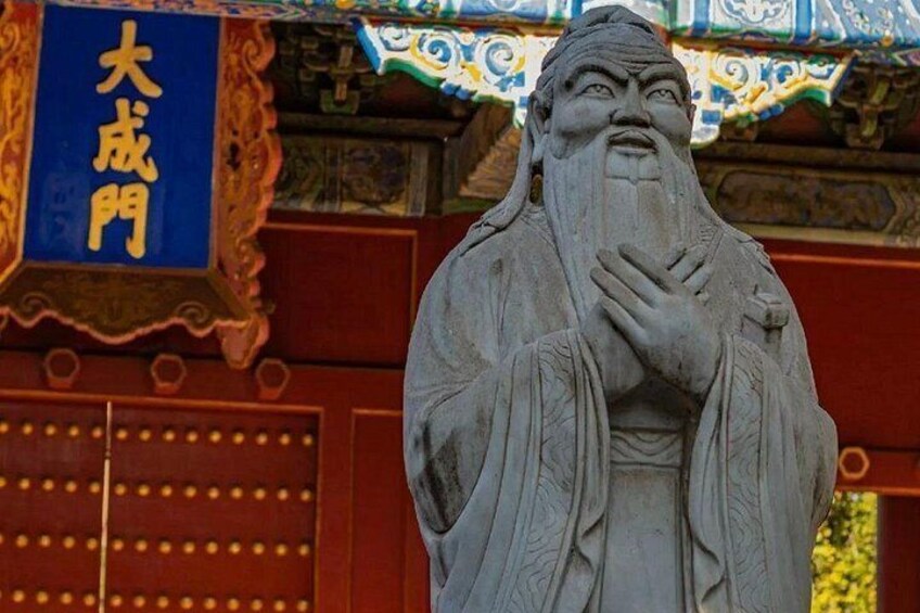 A statue of a robed figure with a long beard, standing in front of a traditional building with a blue sign. 1