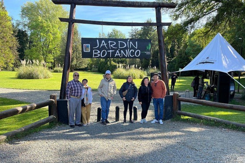 Een groep mensen staat voor een bord met de tekst 'JARDÍN BOTÁNICO', met een tent en een houten hek op de achtergrond. 3