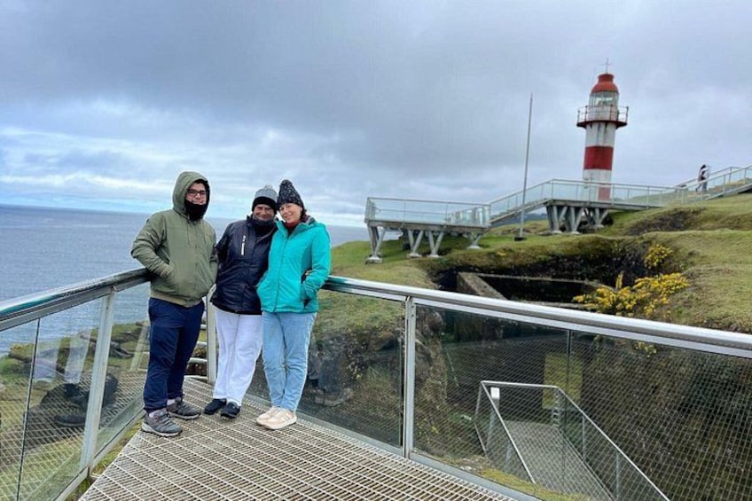 Drie personen staan op een metalen trap met uitzicht op een vuurtoren. 4